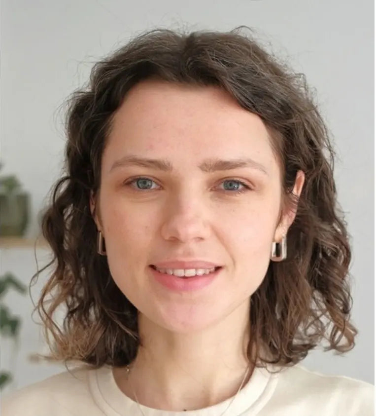 Woman with wavy brown hair wearing a light-colored top against a neutral background